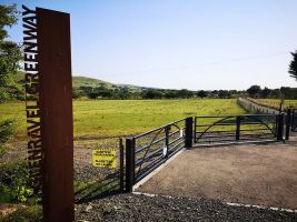 An artistic metal signpost with the words GLENRAVEL GREENWAY rising vertically